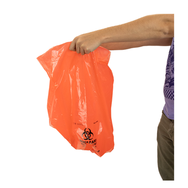 A person in a purple shirt and brown pants holds a bright orange Dynarex Biohazard Waste Bag by the top, with the biohazard symbol and warning text clearly visible for safe containment.