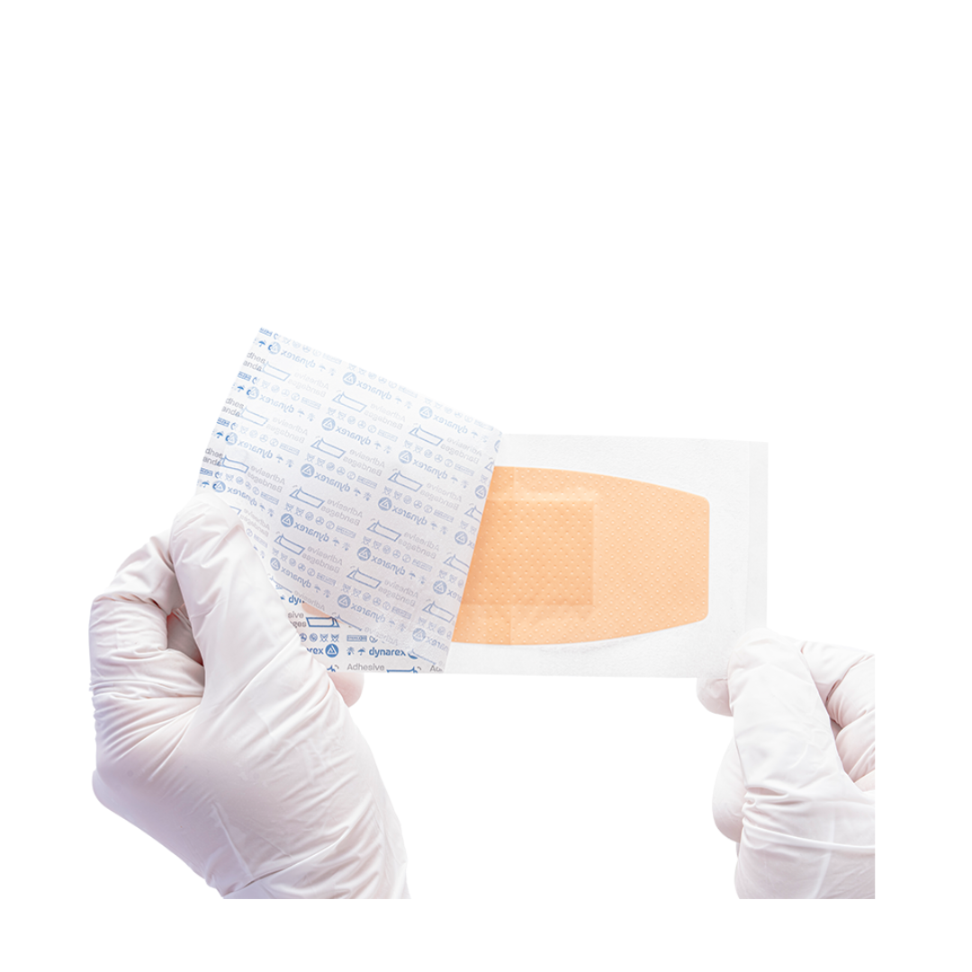 A pair of gloved hands peels open a sterile Dynarex Sheer Plastic Adhesive Bandage, revealing the bandage inside against a white background.