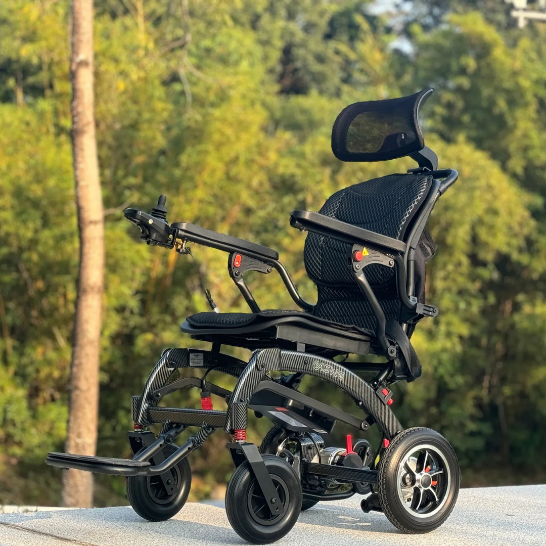 The EASWE B10 Portable Folding Powerchair - Airline Approved, featuring mesh seating, an adjustable headrest, and dual motors in sleek black, is parked outdoors on concrete with sunlight and green trees in the background.