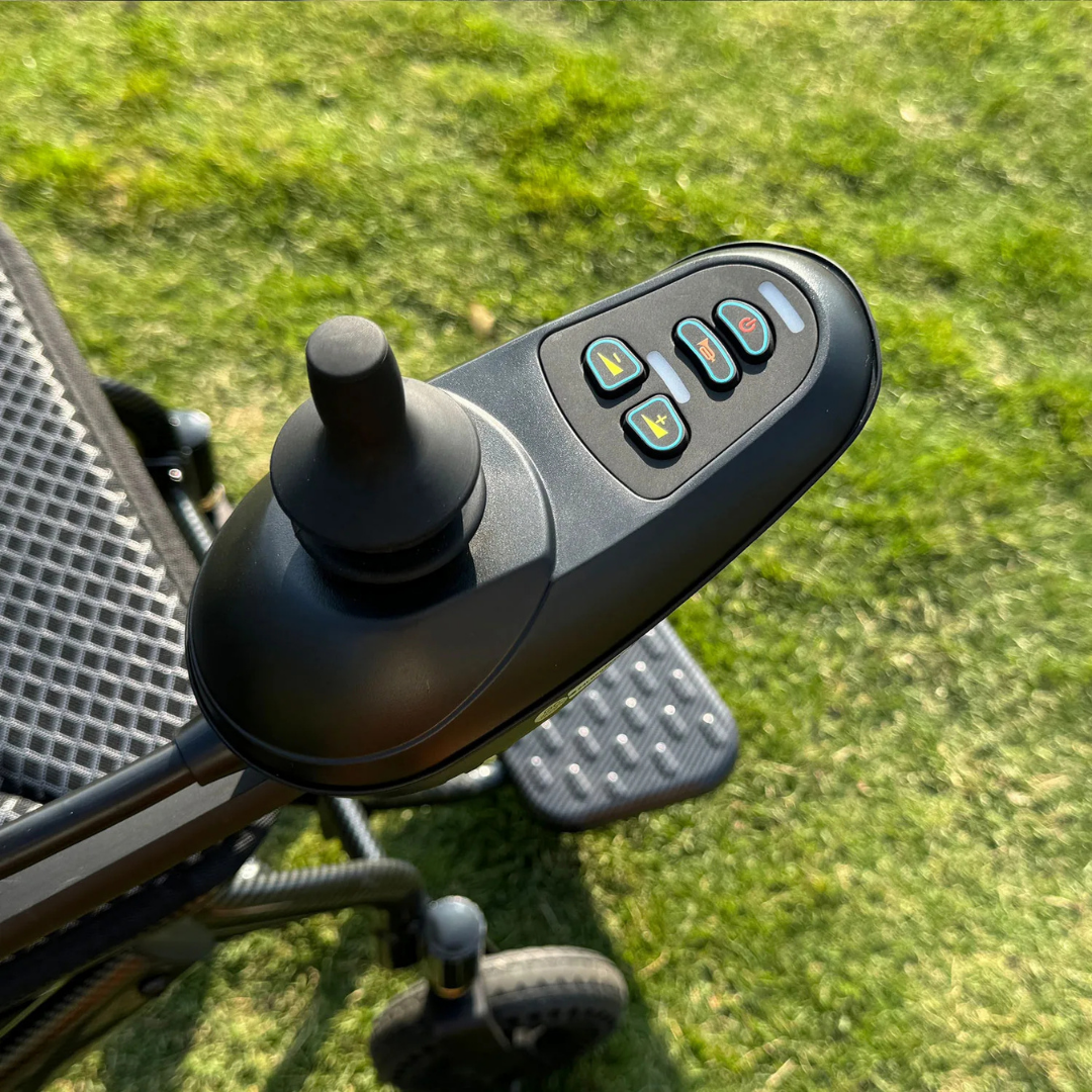 Close-up of the joystick control panel on the EASWE B10 Portable Folding Powerchair - Airline Approved, showing four labeled buttons and a joystick handle, with grass in the background.