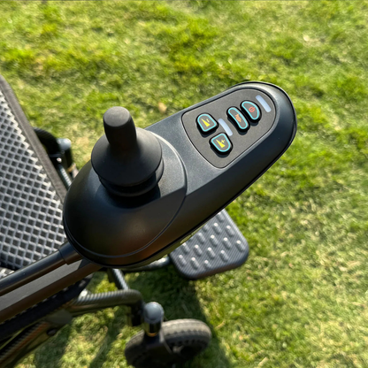 Close-up of the joystick control panel on the EASWE B10 Portable Folding Powerchair - Airline Approved, showing four labeled buttons and a joystick handle, with grass in the background.