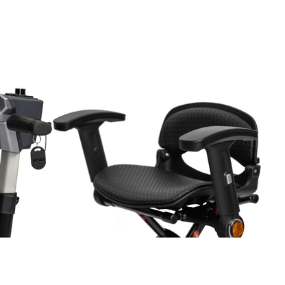 Close-up of the EV Rider Transport 4M Travel Scooter's black seat with armrests and textured cushioning. The lightweight scooter's handlebar and ignition key are visible on the left side of the image.