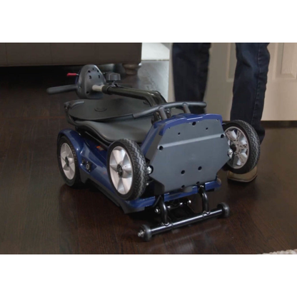A person stands next to the EV Rider Transport AF4W Automatic Folding Mobility Scooter with a high-capacity lithium battery on a dark wood floor, ready for transport or indoor storage.
