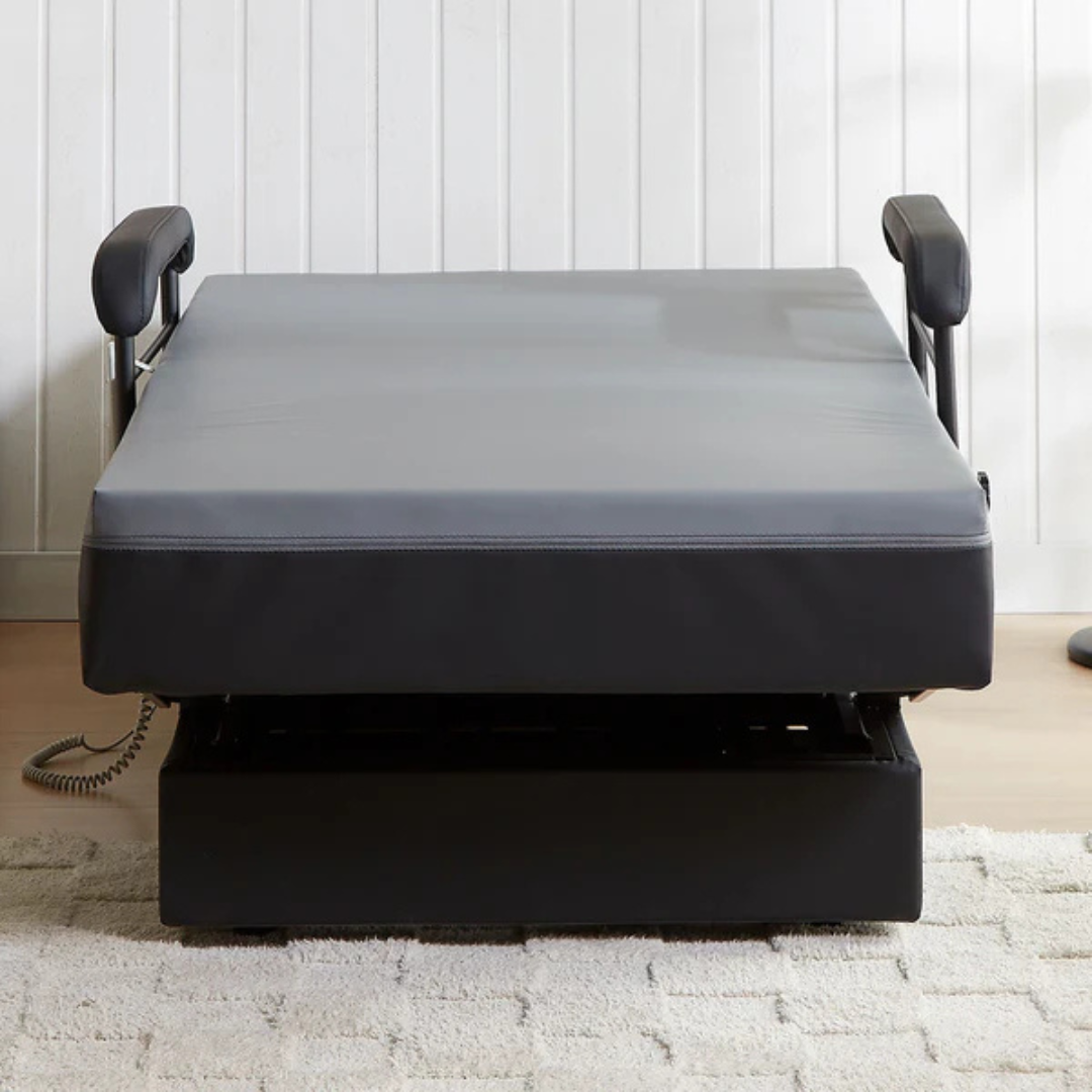 The EZLift Bed Hi-Lo Pro™ Electric Bed with Stand Assist features a gray mattress, black base, and raised side rails, set on a light rug in a room with white paneled walls.