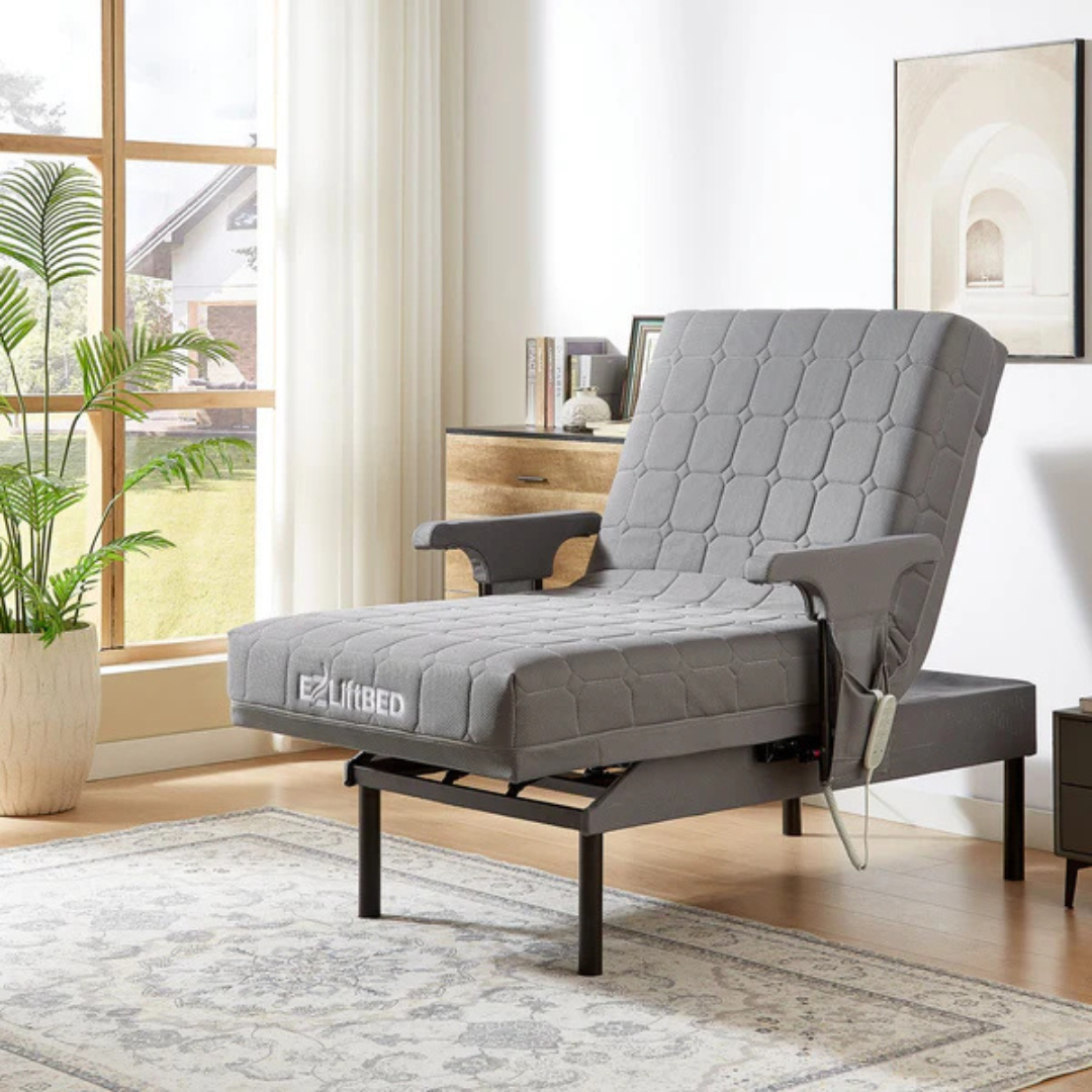 The EZLift Bed™ - Deluxe Sleep To Stand Electric Bed, with armrests and remote, is shown partially reclined in a bright bedroom featuring a large window, plants, dresser, framed art, and a patterned rug.