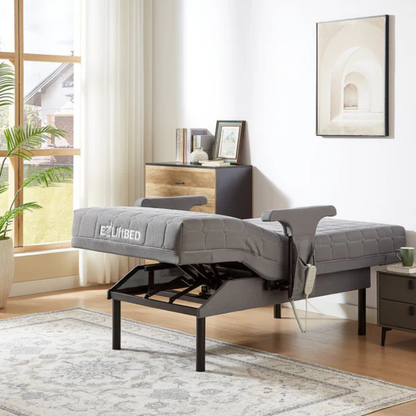 An EZLift Bed™ - Deluxe Sleep To Stand Electric Bed with a gray mattress stands elevated in a bright, stylish bedroom with a rug, nightstand, dresser, wall art, and sunlight streaming through sheer curtains.