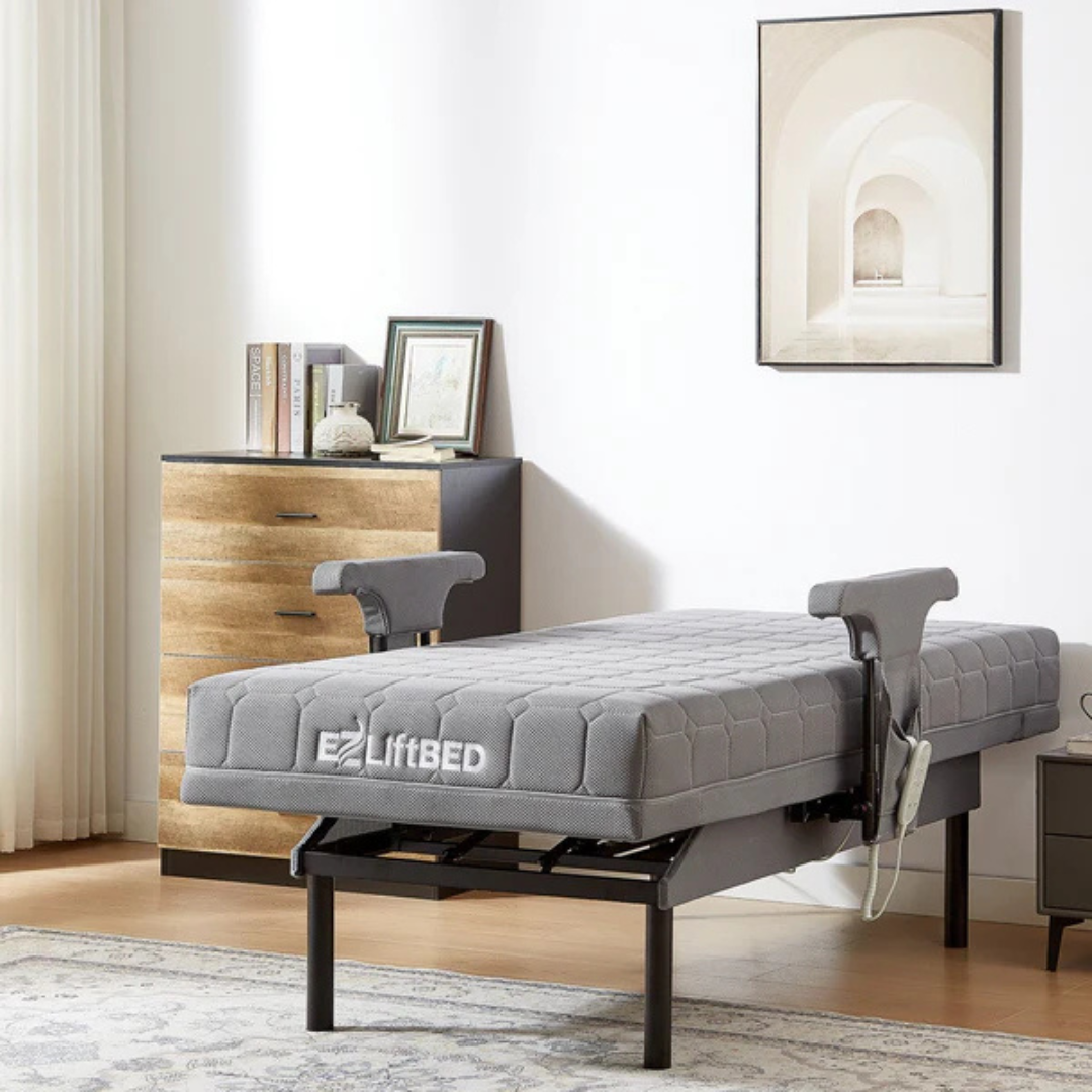 A modern bedroom with the EZLift Bed™ - Deluxe Sleep To Stand Electric Bed with side rails, a wooden dresser with books and décor, a rug, wall art, and sheer white curtains filtering natural light.