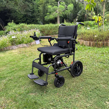An Easwe™ D10 Foldable Electric Wheelchair - FAA Approved, featuring a lightweight black frame and mesh seat, sits empty on green grass in a park with trees, plants, and a wooden fence in the background.
