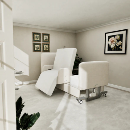 A modern beige reclining chair with wheels sits in a bright, minimalist room with light walls, floral art, framed photos, and plants—perfectly complementing the Elevra Deluxe Rotating Hi-Lo Lift Assist Bed's comfort.