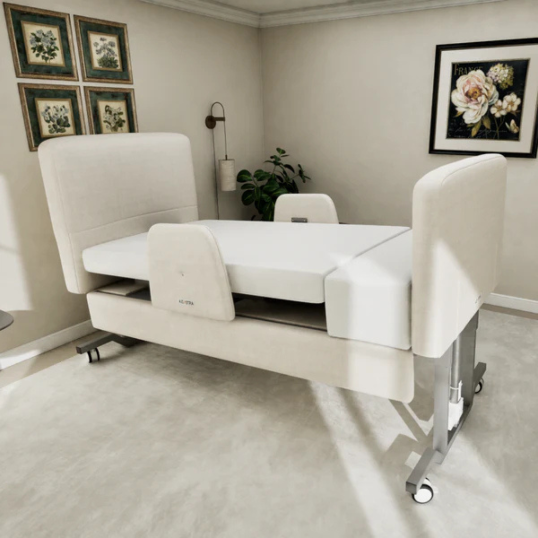 An Elevra Deluxe Rotating Hi-Lo Lift Assist Bed with cream upholstery sits in a bright bedroom, highlighted by framed floral art and a potted plant. Raised head, foot, and side panels enhance comfort.