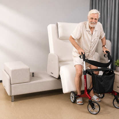 An elderly man with white hair and beard stands using a red walker beside an Elevra Deluxe Rotating Lift Assist Bed - Dual King, a modern light-colored bed with an adjustable, cushioned backrest for advanced homecare.