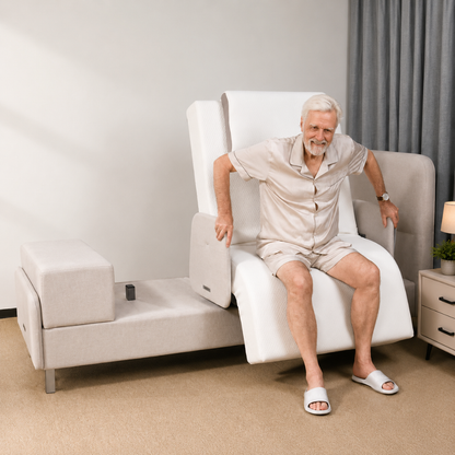 An elderly man in light pajamas sits on the Elevra Deluxe Rotating Lift Assist Bed - Dual King in a modern bedroom, using the raised backrest and armrests to support himself as he rises, smiling and looking comfortable.