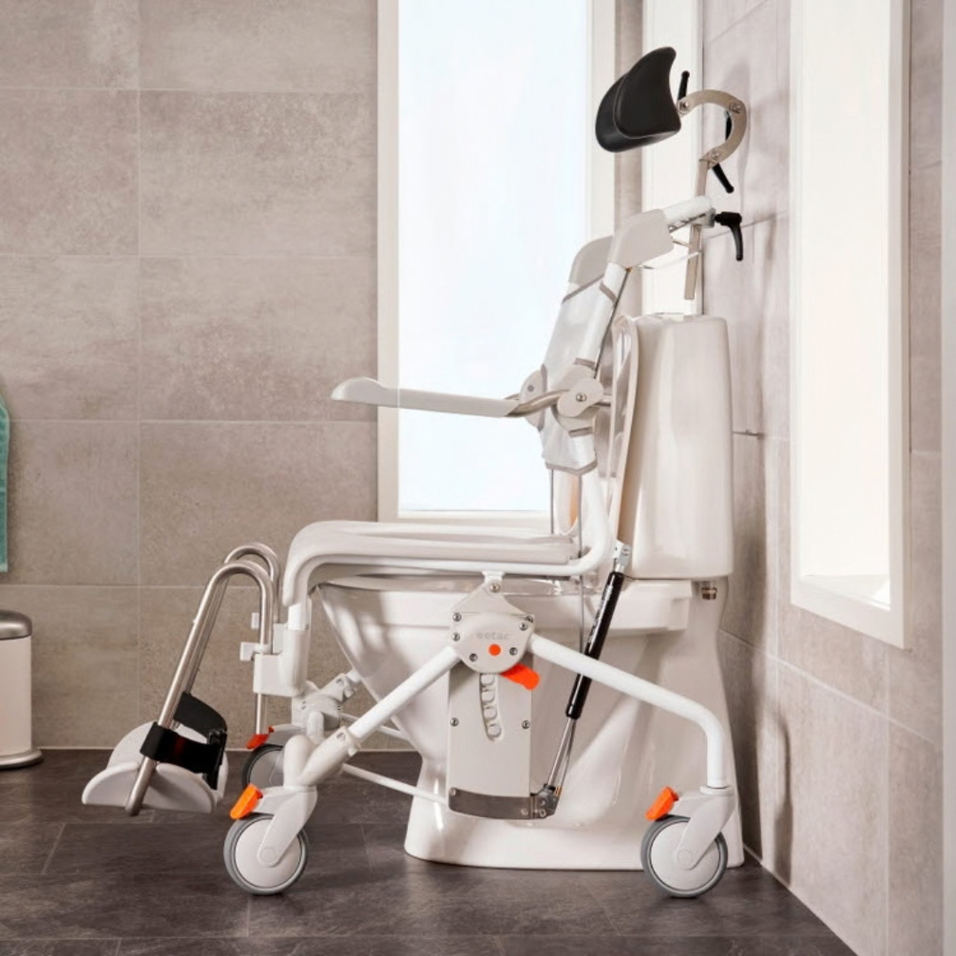 An Etac Swift Mobil Tilt-2 tilt-in-space mobile shower commode chair positioned over a toilet in a bathroom.