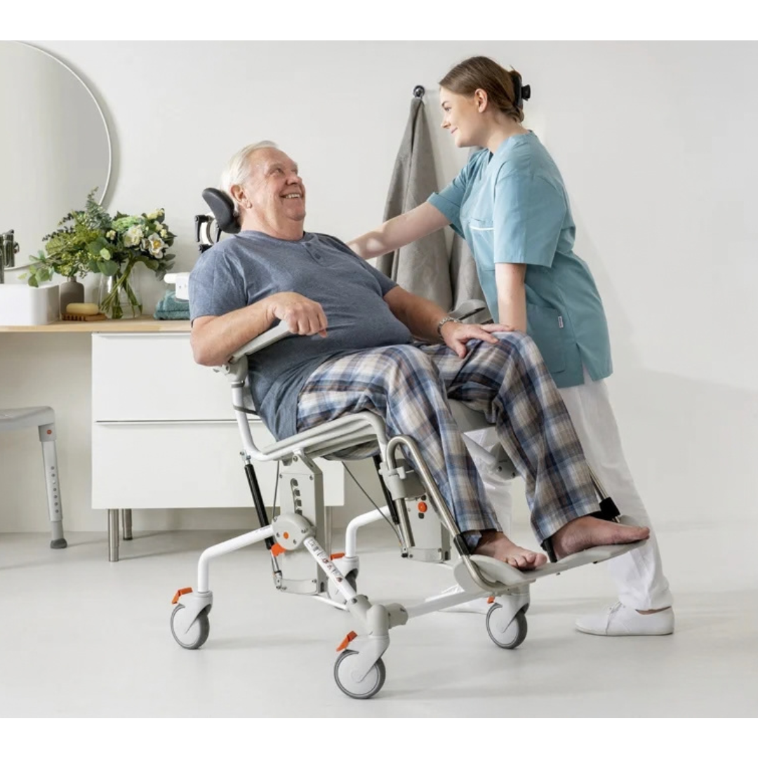 A caregiver assists an elderly man seated in an Etac Swift Mobil Tilt-2 | Tilt-In-Space Mobile Shower Commode.