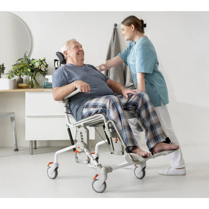 A caregiver assists an elderly man seated in an Etac Swift Mobil Tilt-2 | Tilt-In-Space Mobile Shower Commode.