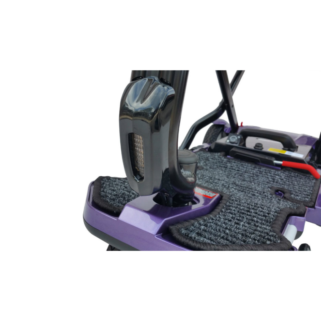 Close-up of the EV Rider Transport Plus Portable Mobility Scooter deck, showcasing textured footrests, a black upright handle, and part of the wheel and frame in the background.