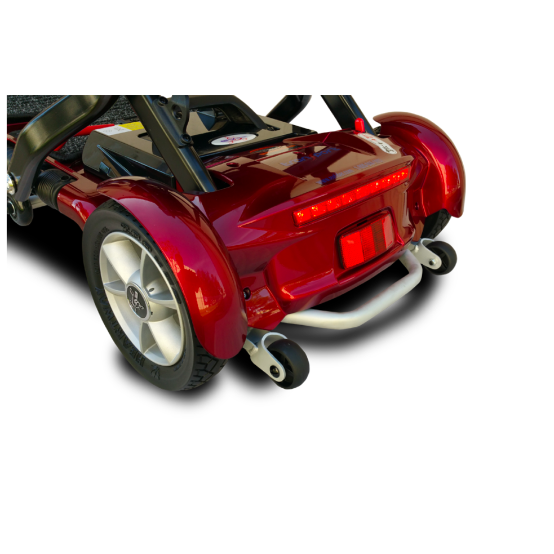 Close-up of the rear section of the EV Rider Transport Plus Portable Mobility Scooter in red, highlighting its rear wheels, metallic bumper, red taillight, and textured footrest against a white background.