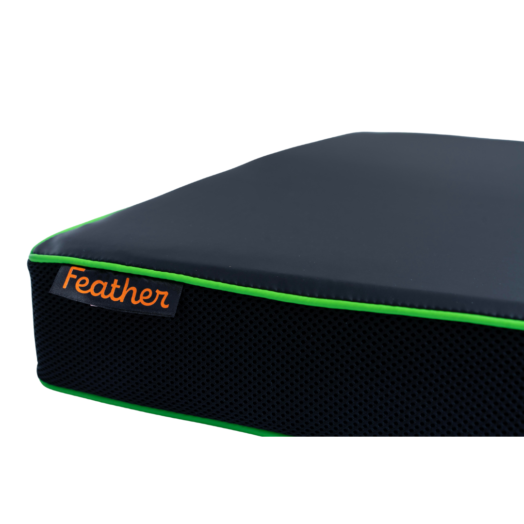 A close-up of a Feather Portable Cushion—an all-purpose black memory foam cushion with bright green piping, an orange Feather label, and a handle—set against a white background.