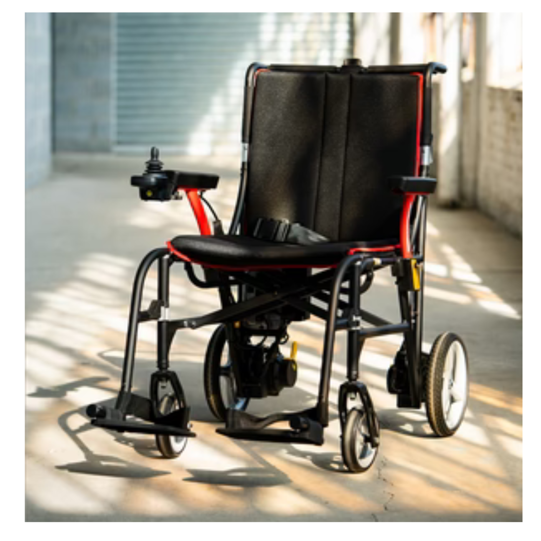 The Feather Powerchair—an ultralight electric wheelchair at just 33 lbs with a black seat, red frame, and joystick control—is parked in a sunlit indoor space with a concrete floor.