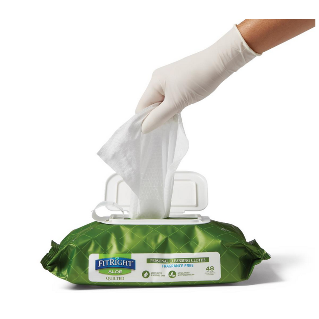 A hand in a white glove pulls a FitRight Aloe Quilted XL Personal Cleansing Wipe from its green, fragrance-free pack, designed for sensitive skin and incontinence care, on a white surface.