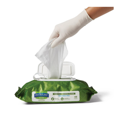 A hand in a white glove pulls a FitRight Aloe Quilted XL Personal Cleansing Wipe from its green, fragrance-free pack, designed for sensitive skin and incontinence care, on a white surface.