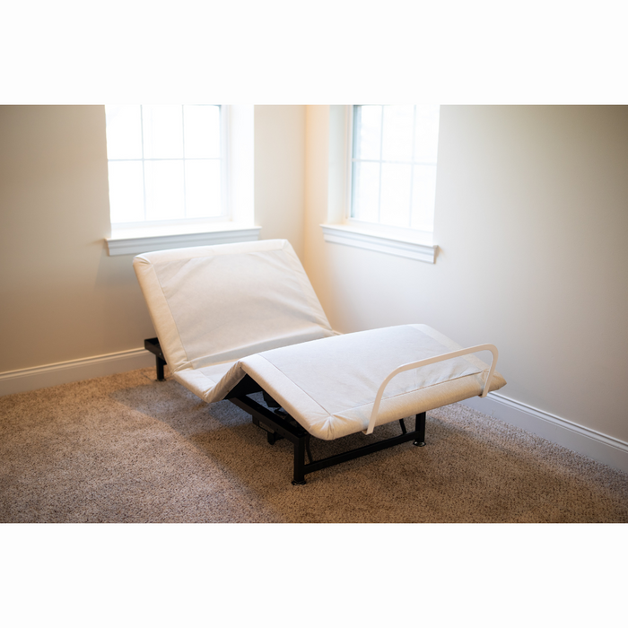 The Flexabed Value-Flex Adjustable Bed, featuring a premier mattress, is arranged in a carpeted room. Its black frame offers adjustable heights, and the head and foot sections are elevated. Light from two white-framed windows enhances the versatility of this sleep solution.