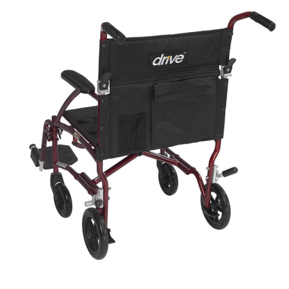 The Drive Fly-Lite Aluminum Transport Chair features a lightweight, foldable metallic red frame, black seat and backrest, armrests, footrests, small black wheels, and a rear storage pocket labeled "drive.