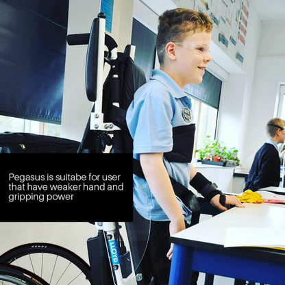 A smiling boy with glasses uses the Foldawheel Lloyd Pegasus Semi-Powered Standing Wheelchair at a classroom desk. Text reads: Pegasus suits users with weaker hand and gripping strength. Another student is visible in the background.