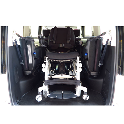 A Foldawheel Lloyd Phoenix 2 Standing Power Wheelchair is secured facing forward in the back of a vehicle, surrounded by safety equipment and support padding on both sides.