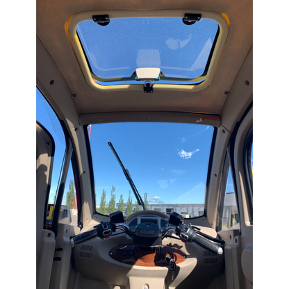 Interior of the GIO Golf Fully Enclosed Mobility Scooter with Heater and Cooling Fan, showcasing handlebars, dashboard controls, and a sunroof above, with blue sky and buildings visible through the windshield.