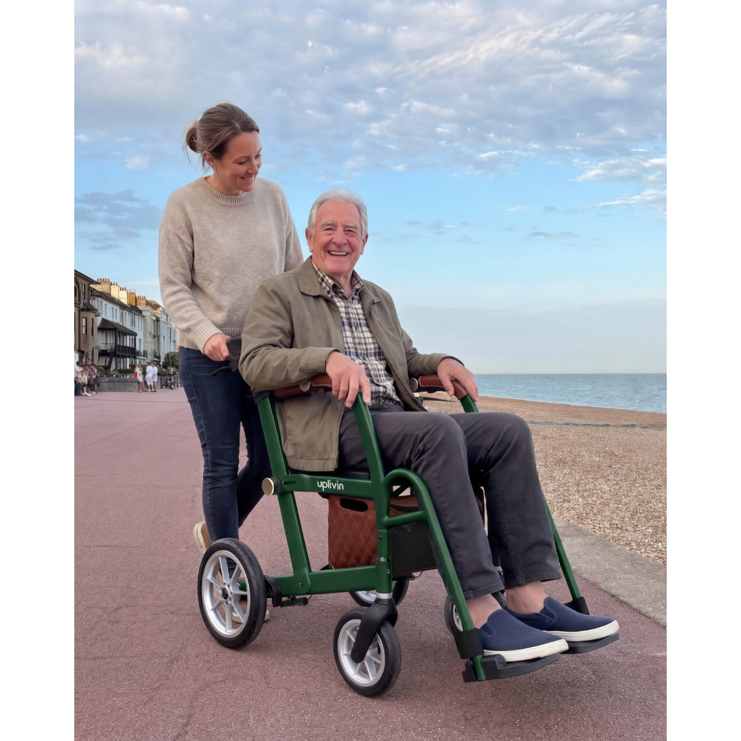 A woman pushes a smiling man sitting in a green uplivin Gavo 2-in-1 Hybrid Rollator & Wheelchair along a seaside promenade.