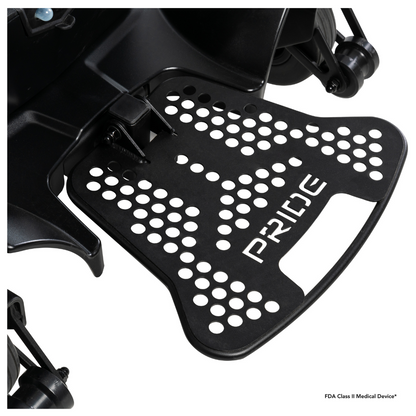 Close-up of a black metal footrest with circular holes and "PRIDE" cut out, attached to the Pride Mobility Go Chair® MED Portable Powerchair; wheels and part of the frame are visible in the background.