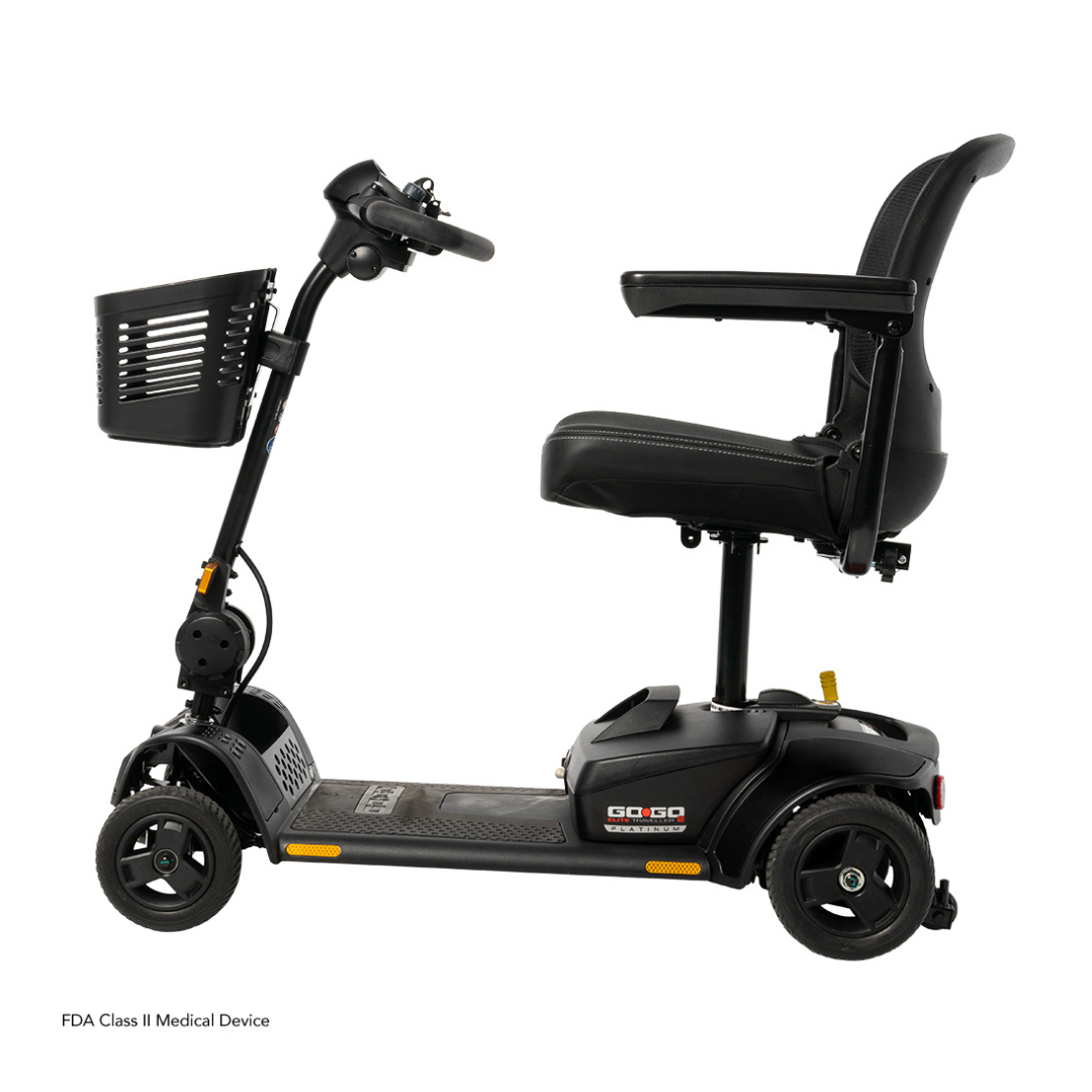 The Pride Mobility Go Go Elite Traveller® 2 Platinum Scooter, in black with three wheels, padded seat, armrests, front basket, and handlebar control panel, is shown from the side against a white background.