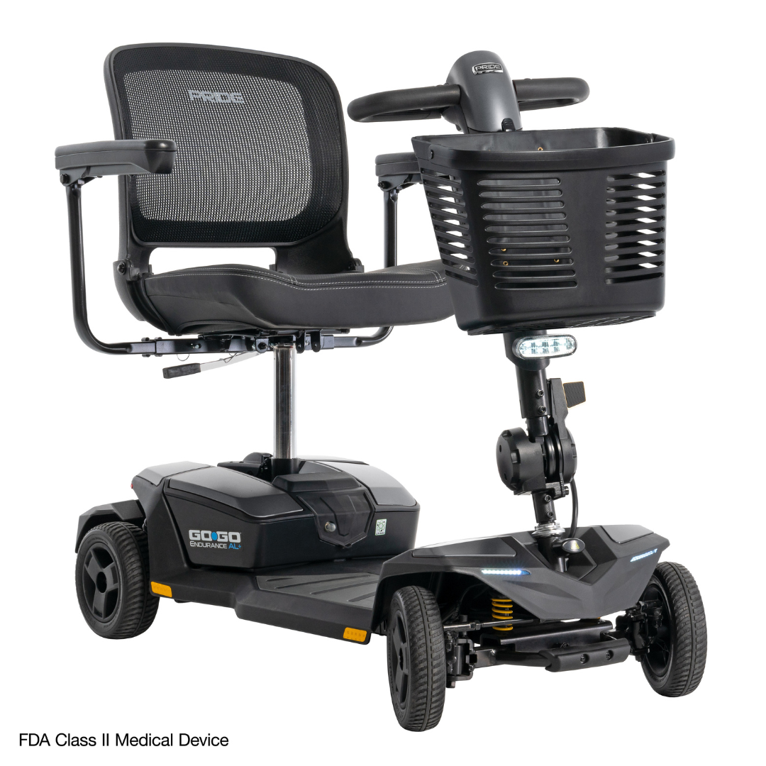 The Pride Mobility Go Go® Endurance AL+ Power Scooter is a black, four-wheel scooter with a mesh seat, front basket, handlebars, compact grid design, Inter font labels, and a small light under the basket for visibility.