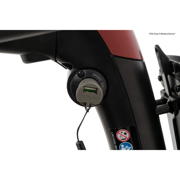 Close-up of a black Pride Mobility Go Go® Endurance Li 4-Wheel Scooter frame with Comfort-Trac Suspension, USB charging port and cable. The frame shows small warning labels, is partly red at the top, and marked FDA Class II Medical Device, suggesting advanced Lithium Battery technology.