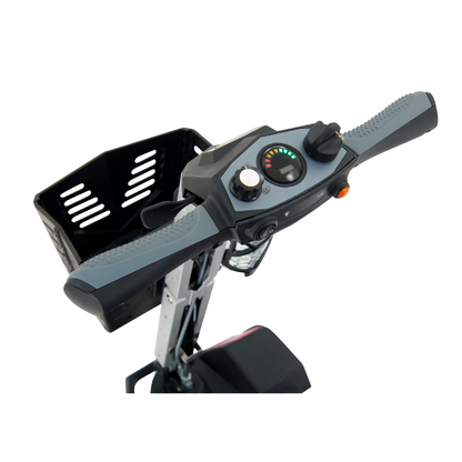The image showcases the handle and control panel of the Golden Technologies Portable Buzzaround GB120 Carry-On Travel Scooter. The handlebars have gray grips, and the panel features a speedometer and controls. A small basket is attached at the front, complementing its fold-flat design for convenience.