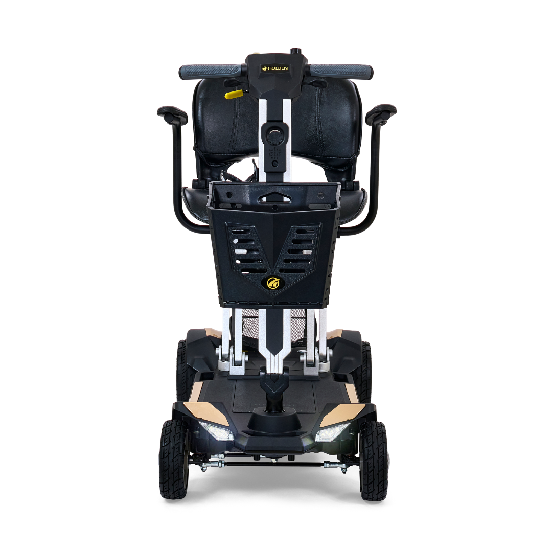 Introducing the Golden Technologies Portable Buzzaround GB120 Carry-On Travel Scooter, a black and silver fold-flat scooter with a sturdy frame. This model features a padded seat with armrests and four wheels for enhanced stability. The handlebars come equipped with an intuitive control panel, while the front basket offers convenient storage solutions. Its design emphasizes compactness and ultra-portability, complemented by a durable lithium-ion battery for extended use.