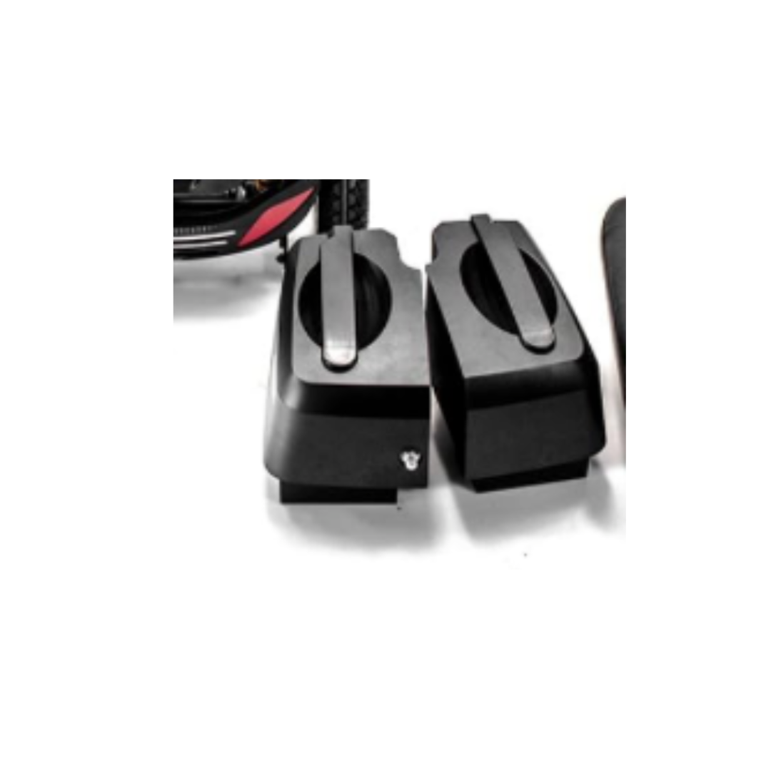 Two black hard-shell motorcycle saddlebags sit side by side on a white surface, with part of a motorcycle and the Golden Battery Pack with Battery Case for Buzzaround Scooters visible in the upper left corner.