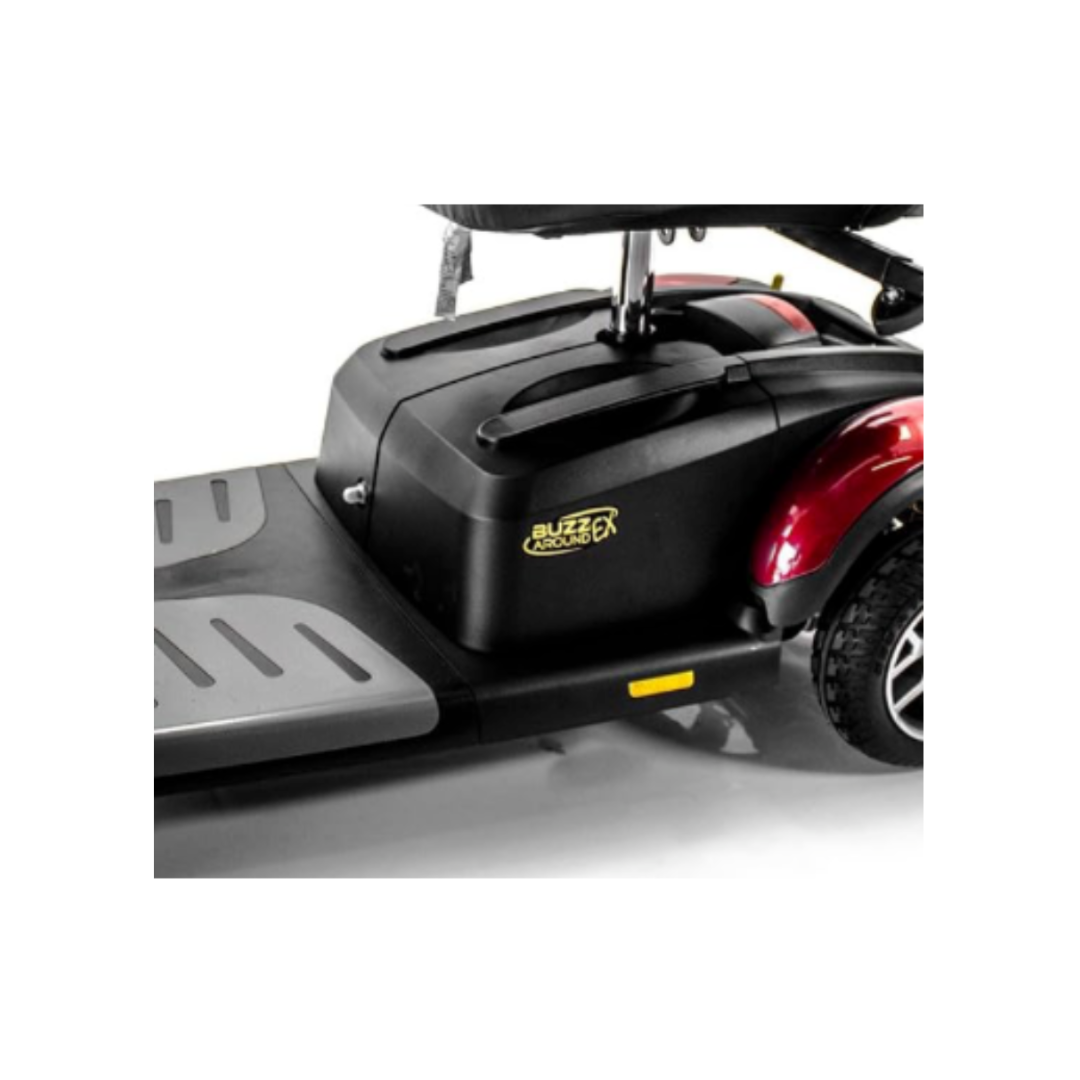 Close-up of a black Buzzaround scooter base featuring the Golden Battery Pack with Battery Case, gray footrests, yellow label, red wheel fender, and space for 12V 12Ah sealed lead-acid batteries.