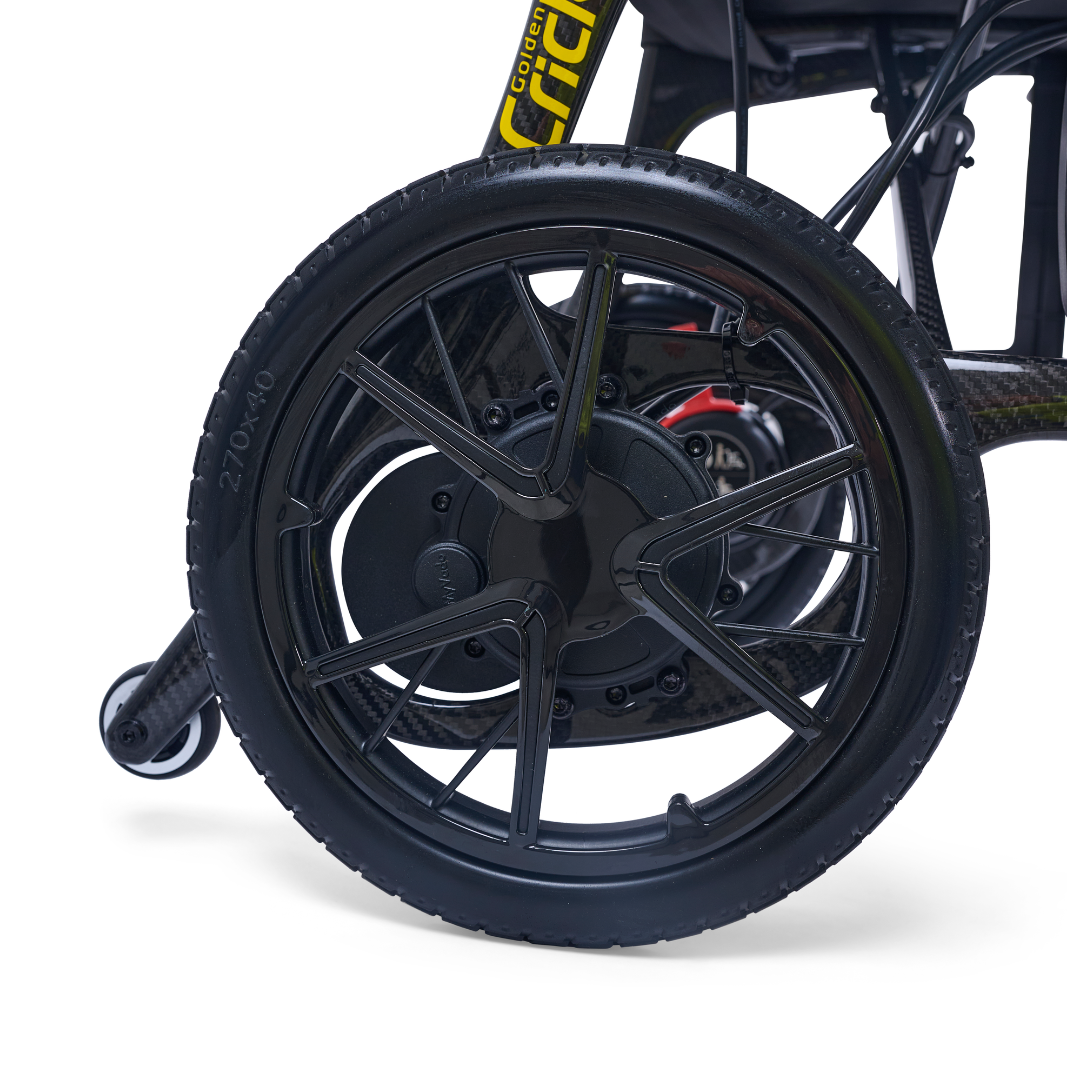Close-up of a black wheel on the Golden Cricket™ LT Carbon Portable Lightweight Powerchair—only 25 lbs—showing detailed spokes and tire tread. The plain white background highlights its lightweight carbon design for exceptional freedom.