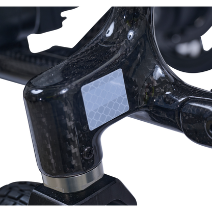 Close-up of the Golden Cricket™ LT Carbon Portable Lightweight Powerchair's glossy carbon fiber frame, featuring a small reflective hex-pattern sticker, highlighting its ultra-light 25 lb design for exceptional portability and freedom.