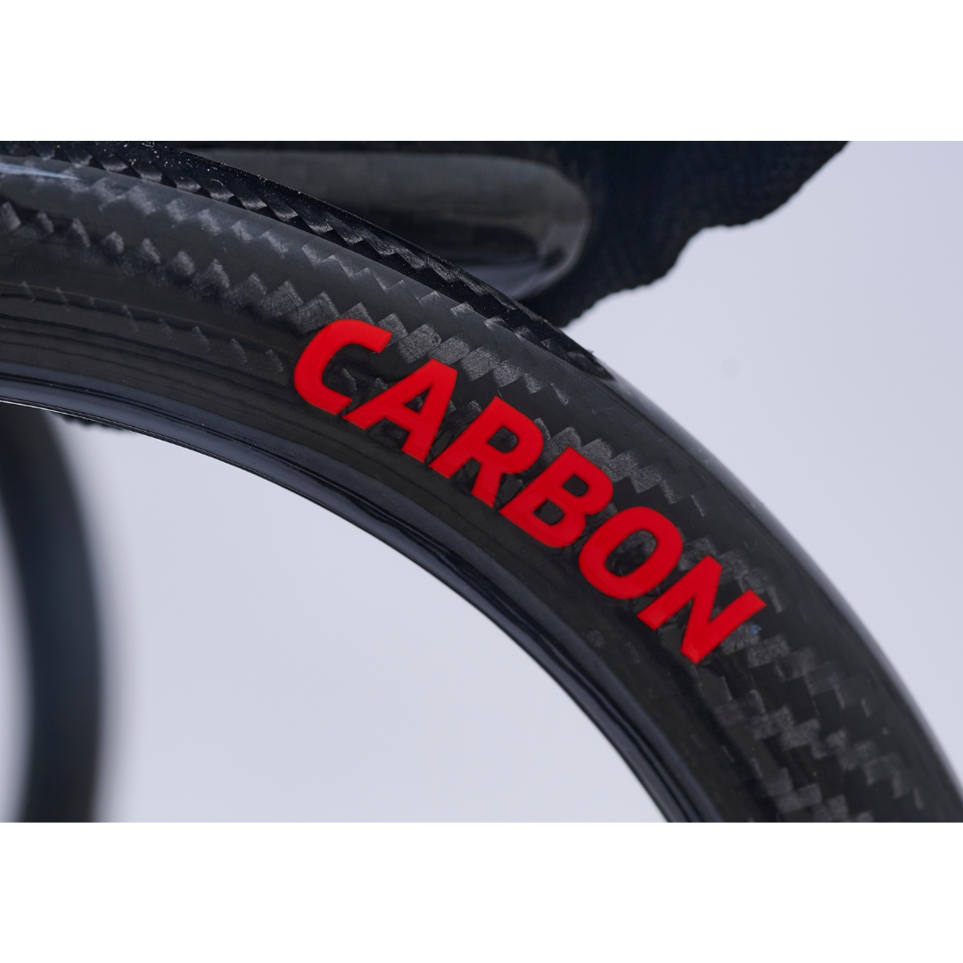 Close-up of the Golden Cricket™ LT Carbon Portable Lightweight Powerchair (only 25 lbs) wheel with CARBON in bold red. The blurred background accents its advanced, lightweight carbon design and exceptional portability.