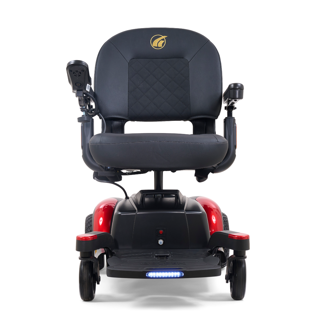 Front view of the Golden Tech BuzzAbout Portable Power Wheelchair, showcasing a black and red design with a cushioned seat, armrests, joystick control, and an LED light at the bottom front.