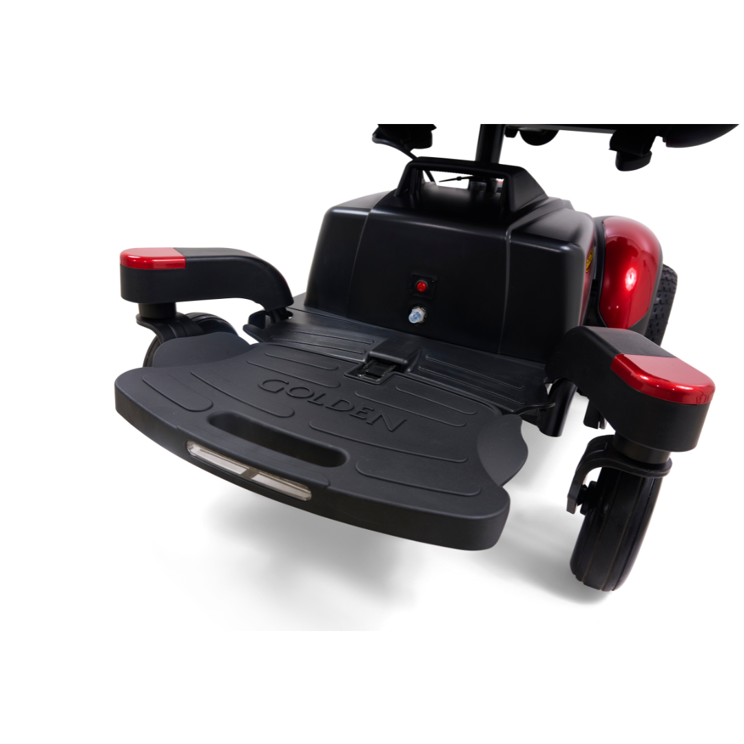 Close-up of the footrest area on a Golden Tech BuzzAbout Portable Power Wheelchair, with "GOLDEN" engraved on the black platform, red armrests, and partially visible wheels.