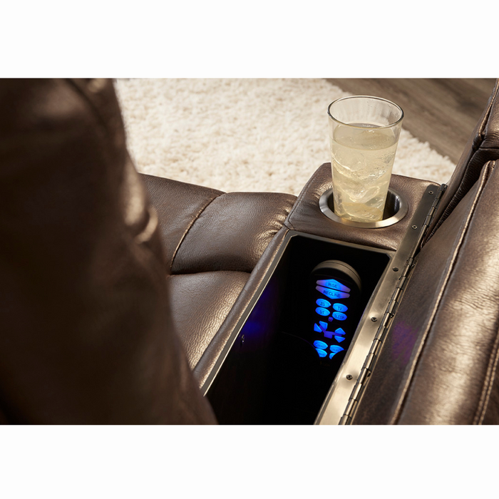 A glass with a light beverage sits in the cup holder of the Golden Tech Rhea PR442 MaxiComfort Recliners brown leather seat, near its glowing blue 4-Zone Comfort Zone panel inside an armrest compartment, next to a light carpet and USB port for convenience.