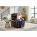 An elderly woman relaxes on a Golden Cloud+ PR511 Recliner with Lift Assist - Medium Wide, resting a cup on an attached tray. She wears a pink sweater and blue jeans in a modern living room featuring side tables, plants, and large windows. The AutoDrive hand control offers personalized comfort in her 4-Zone Comfort Zone chair.