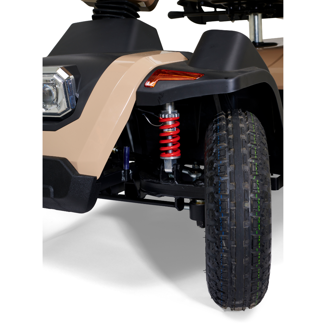 Close-up of the Golden Tech Eagle HD Bariatric 4-Wheel Scooters front wheel, highlighting the off-road tire tread. The tan vehicle features a black wheel arch, red suspension spring, and a gleaming headlight, perfect for outdoor adventures.
