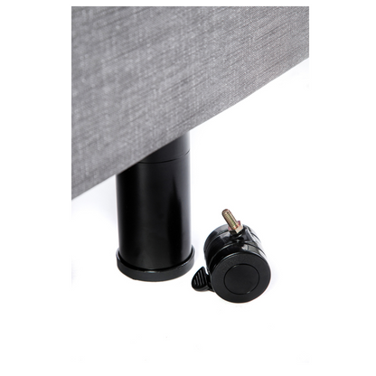 A black cylindrical bed leg from Golden Tech Passport stands upright, attached to gray upholstered furniture for safety and functionality, while a similarly colored caster wheel lies on its side, exemplifying high-quality homecare bed accessories against a white background.