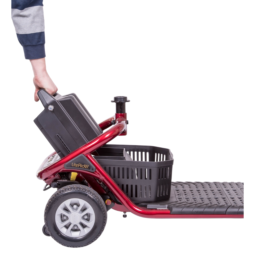 A person holds the handle of a red Golden Tech GL111 LiteRider 3-Wheel Mobility Scooters battery compartment, designed for easy wireless disassembly. The scooter features a black basket between its delta tiller handlebars and wheels, shown in side profile against a white background.