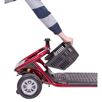 A person in a striped sleeve attaches a black basket to the front of a red Golden Tech GL111 LiteRider 3-Wheel Mobility Scooter, showcasing its logo on the frame. The scooter has a visible wheel and footrest, designed for easy wireless disassembly.